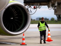 Airport worker moves cones near an airplane on a runway