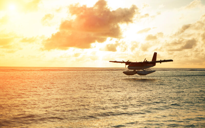 A seaplane flying by a sunset