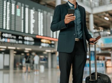 Young businessman at timetable screen board using smart phone.Flight board.