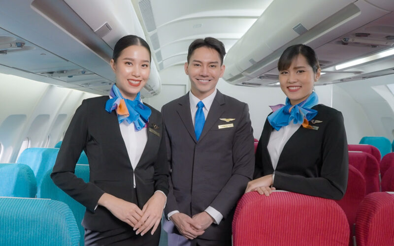 Portrait of three man and woman in blue suit flight attendant air hostess in economy class cabin smiling to welcome passenger at airplane