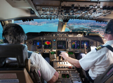 The cockpit of modern jet airplane. Aircraft flies above the city landscape and river. Pilots at work.