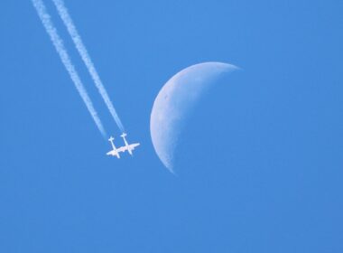 Virgin Galactic VMS Eve flies in a blue sky with the moon in the background