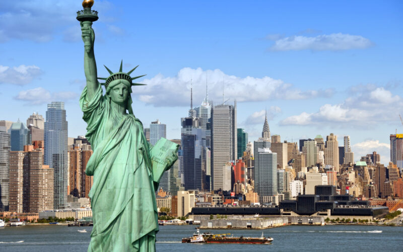 new york city skyline cityscape with statue of liberty over hudson river with midtown Manhattan skyscrapers and freight sailing ship in usa america